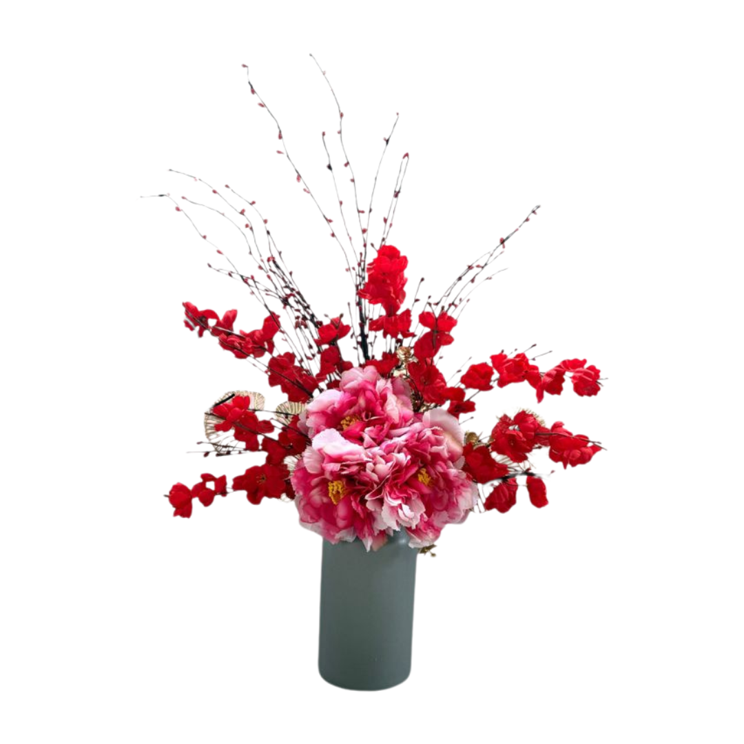 Vibrant floral arrangement featuring bright red flowers and a large pink peony bouquet in a grey cylindrical vase, set against a white background.