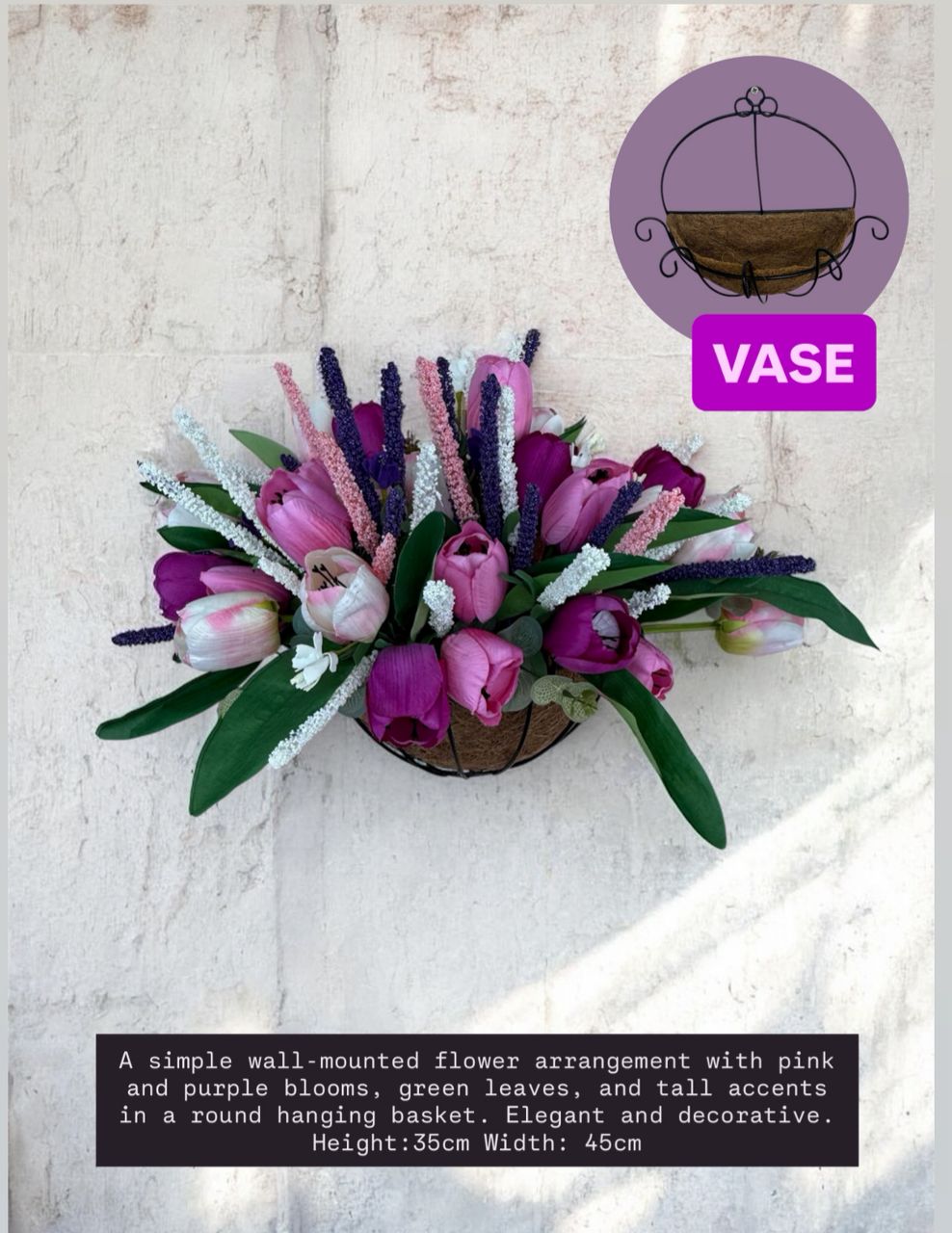 Wall-mounted flower arrangement with pink and purple blooms in a round hanging basket on a light background.