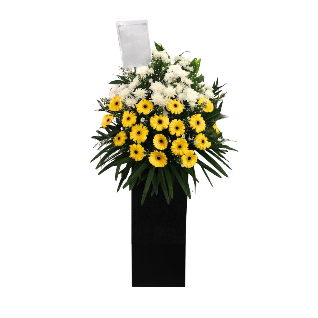 Tall flower stand with yellow gerberas, white chrysanthemums, and tropical leaves in a black base for a business grand opening or condolence event.