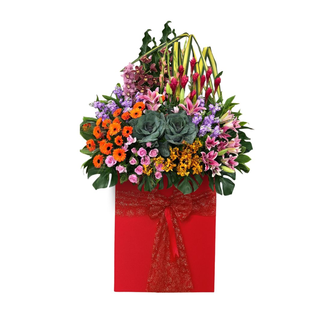 Vibrant, tall grand opening flower stand with orange and red gerberas, pink lilies, purple orchids, and brassicas in a decorative red box base, used to celebrate new business ventures or achievements in Singapore.
