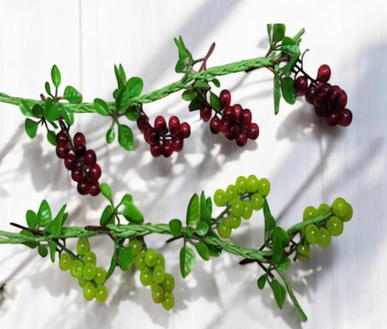 Two strings of artificial grapes, one red and one green, with small leaves and wrapped stems.