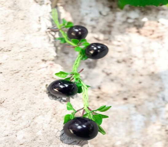 Artificial green vine with black berries on a textured surface