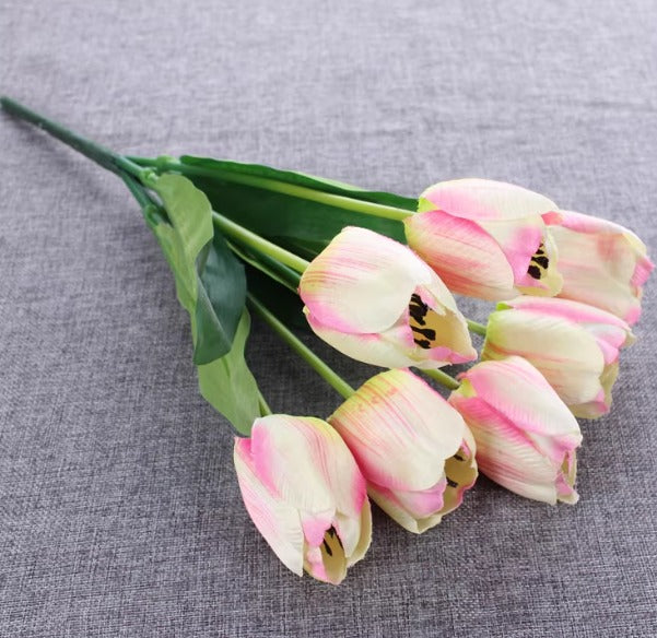 Artificial white and pink tulip bouquet with green leaves on a gray fabric surface.