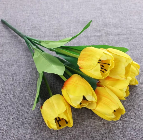 Artificial yellow tulip bouquet with green leaves.