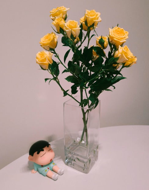Clear vase with yellow flowers on a white surface next to a small figurine.