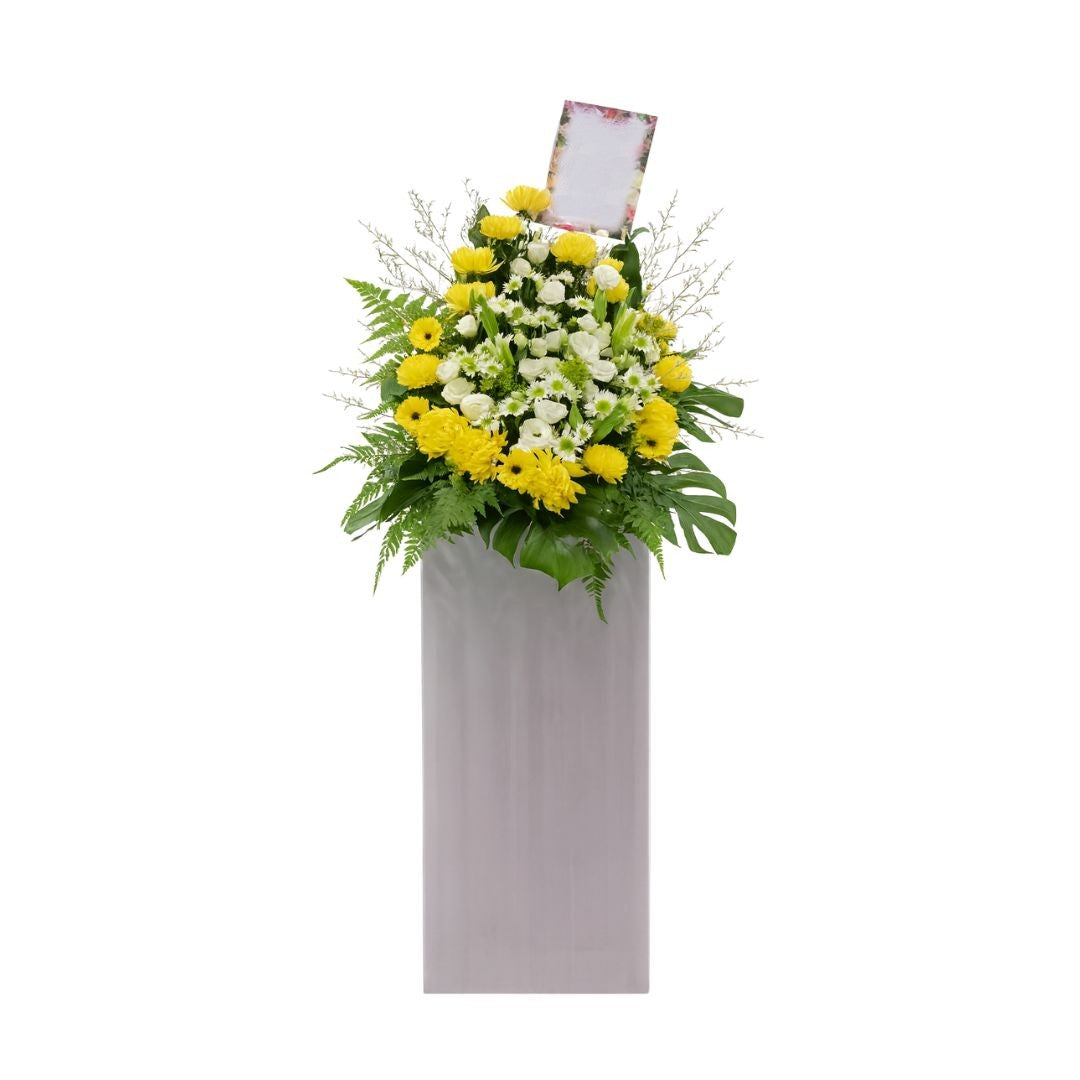 Floral condolences arrangement in a gray container with a photo frame on a white background