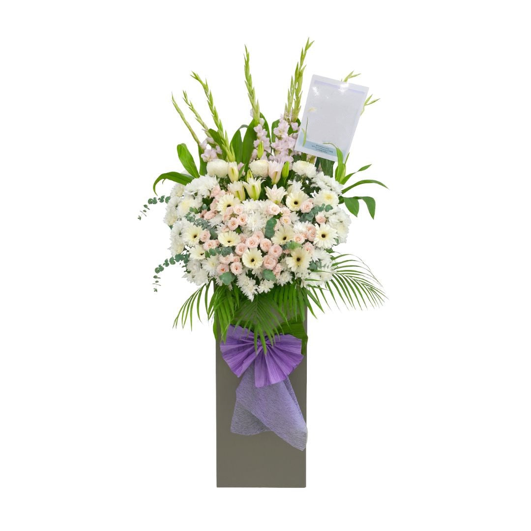 Floral condolences arrangement with a purple bow on a white background