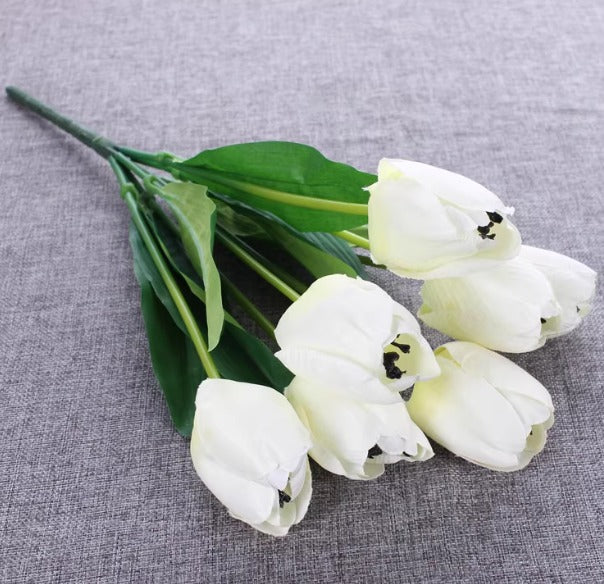 Artificial white tulip bouquet with green leaves.